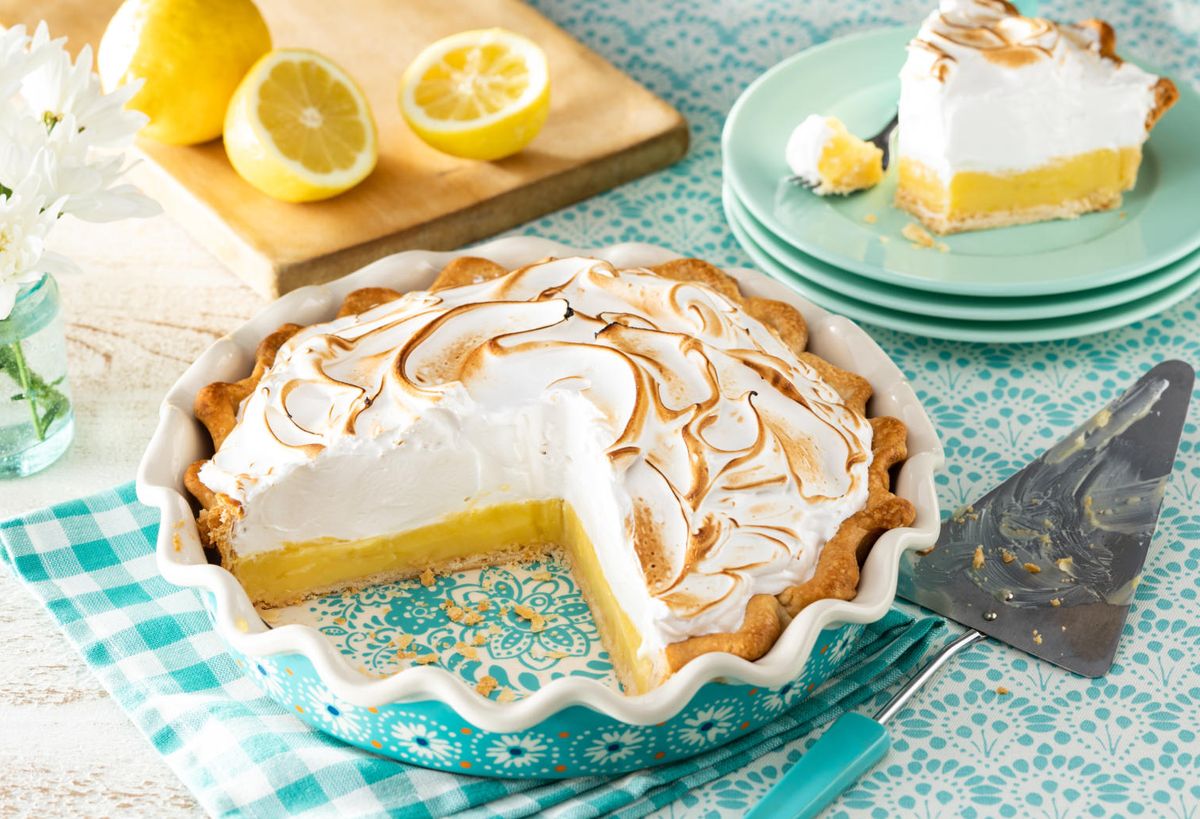 classic lemon meringue pie with slice cut out and lemon slices