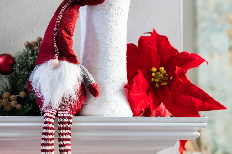 a classic norweigan holiday christmas gnome decoration sitting on a white modern mantle with a white vase with eucalyptus and a poinsettia bloom