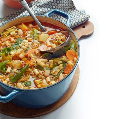 classic minestrone soup with a ladle in a blue dutch oven on a wooden board