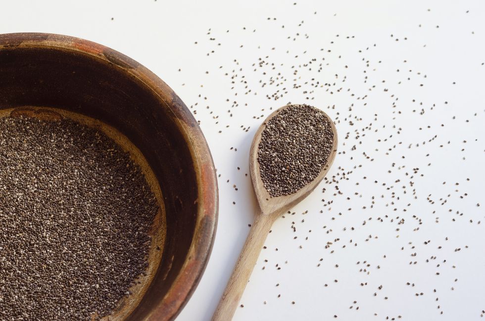clay vessel and wooden spoon with chia seeds on white background, seeds scattered on the table