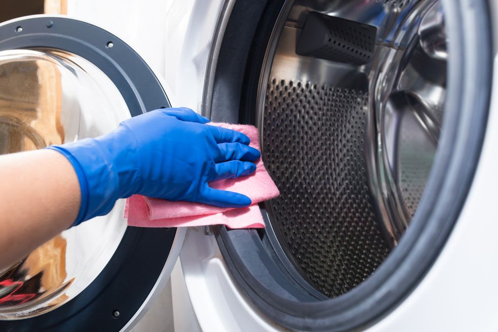hands in blue rubber gloves wiping down the rubber gasket on a washing machine where it meets the door