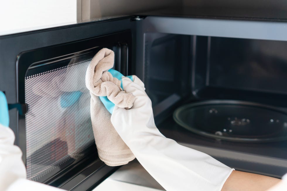 woman hand with microfiber rag cleaning inside of microwave oven in kitchen at home closeup