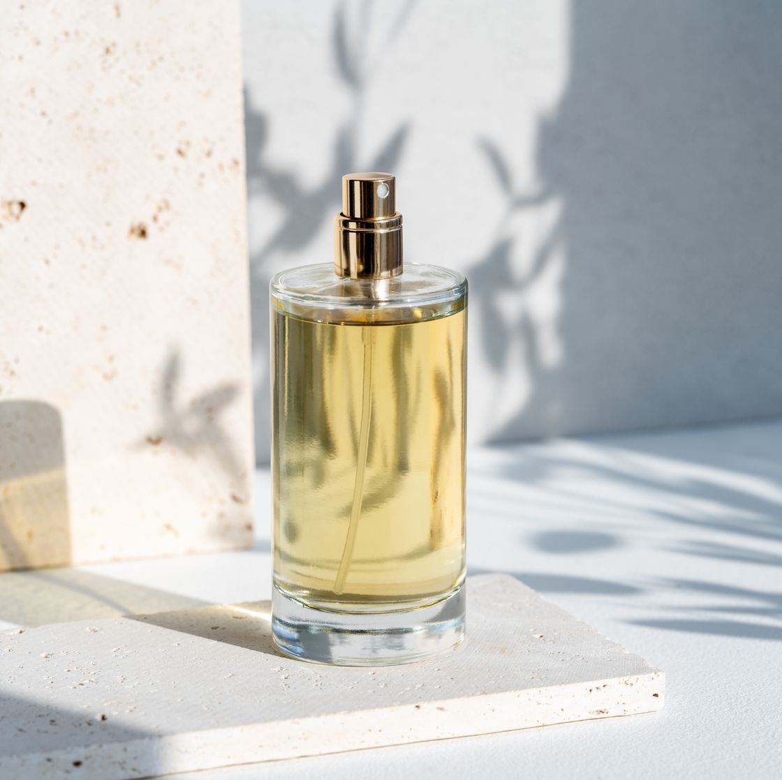 Uma garrafa de vidro transparente com perfume é elegantemente exibida em uma mesa branca, pegando o brilho suave da luz solar natural.