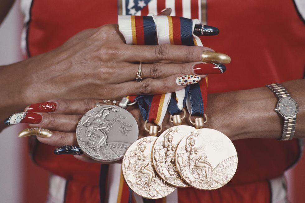 florence joyners hands hold four medals on red, white, blue and yellow striped ribbons, her long nails are bejeweled and painted several colors