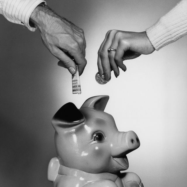 CLOSE-UP COUPLE PLACING MONEY IN PIGGY BANK