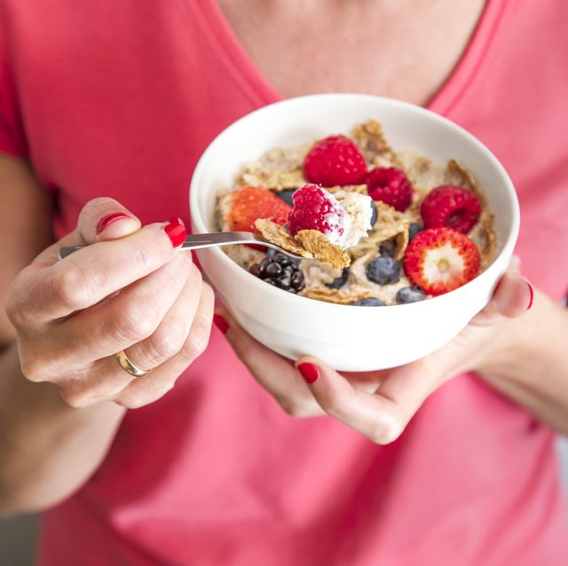 close up crop of woman holding a bowl containing homemade granola or muesli with oat flakes, corn flakes, dried fruits with fresh berries healthy breakfast