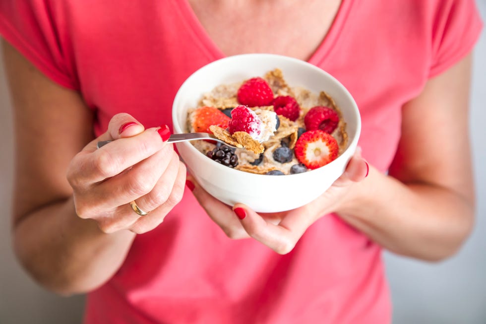 close up crop of woman holding a bowl containing homemade granola or muesli with oat flakes, corn flakes, dried fruits with fresh berries healthy breakfast