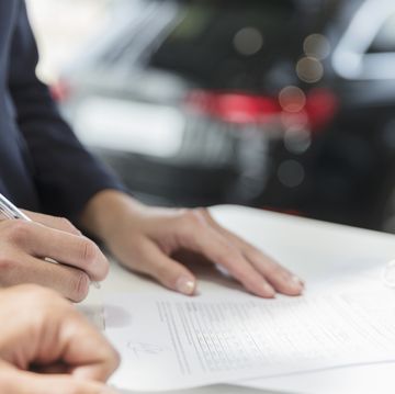 Close up customer signing financial contract paperwork in car dealership
