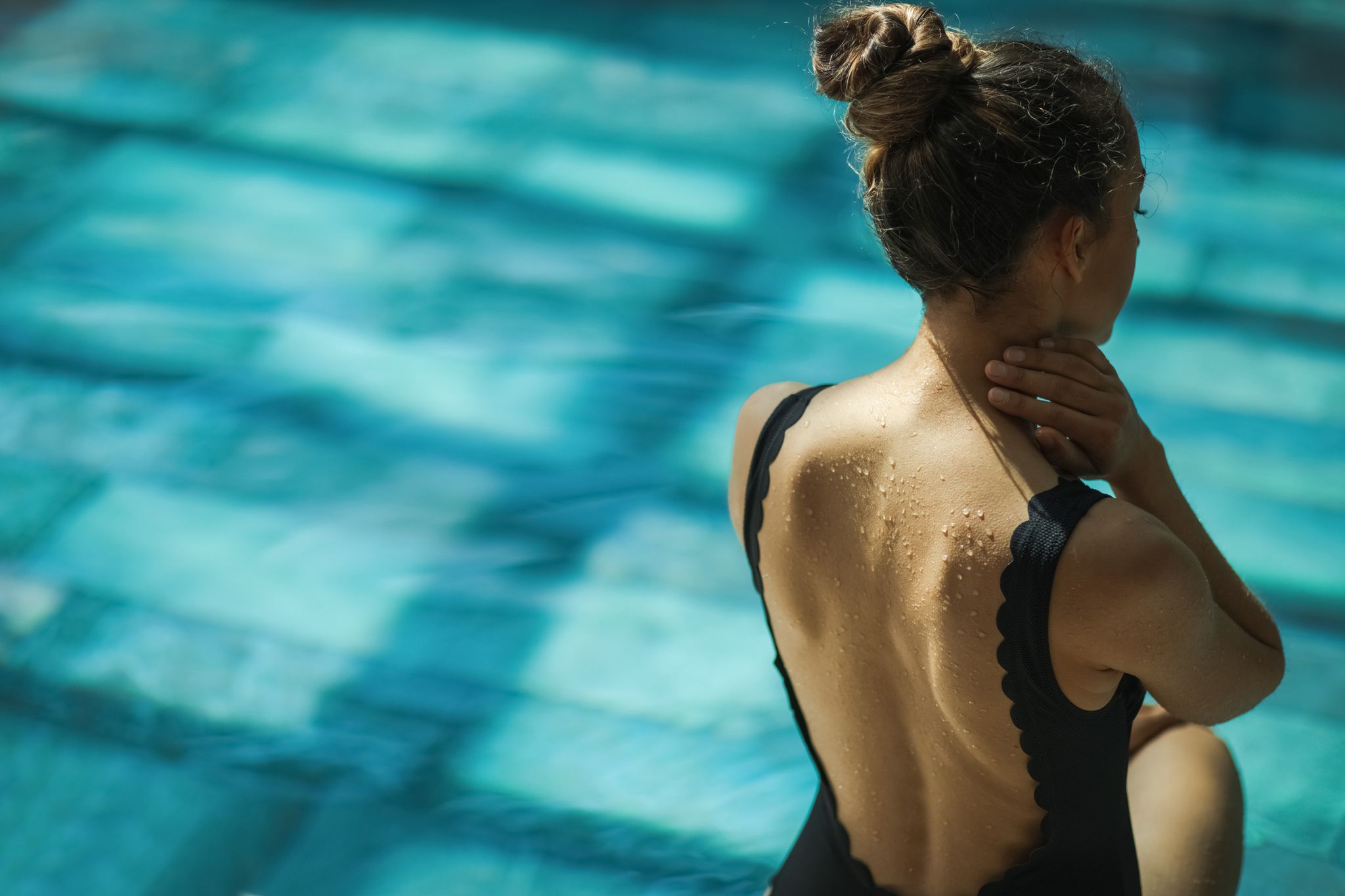 close up details of woman back with water drops on background of swimming pool sensual details of body in water