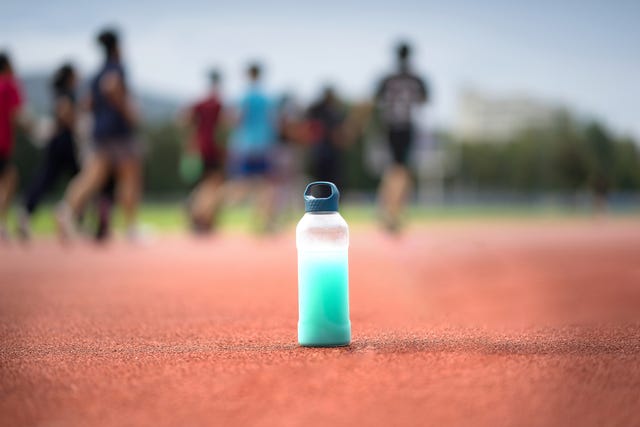 bebida isotónica en primer plano y en el fondo corredores en una pista de atletismo