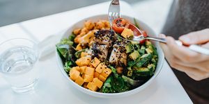 close up, high angle shot of young woman enjoying multi coloured healthy fruit, vegetables with grilled chicken salad bowl with balanced nutrition in cafe, with a glass of water by the side healthy eating lifestyle people, food and lifestyle concept