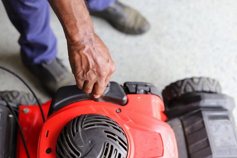 a close up image of an african american man adding gasoline in a lawnmower
