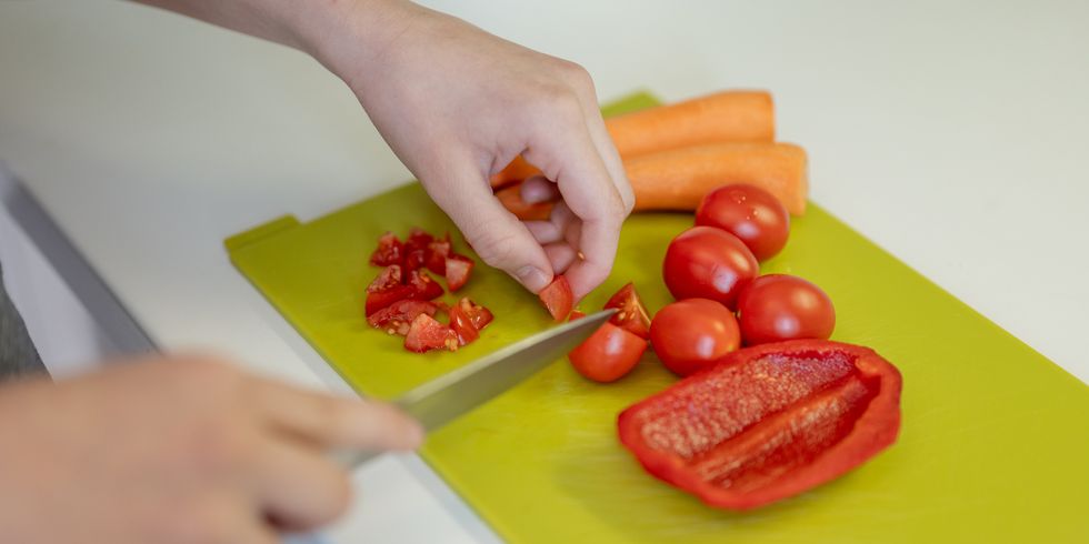 close up image of young hands cutting tomatoes, carrot and paprika on a cutting board