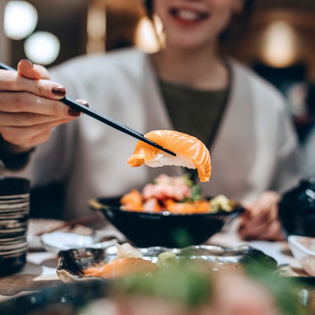 close up, mid section of smiling young asian woman enjoying delicate freshly served sushi with chopsticks in japanese restaurant, sharing assorted authentic japanese cuisine with friends while dining out asian cuisine and food people and food concept