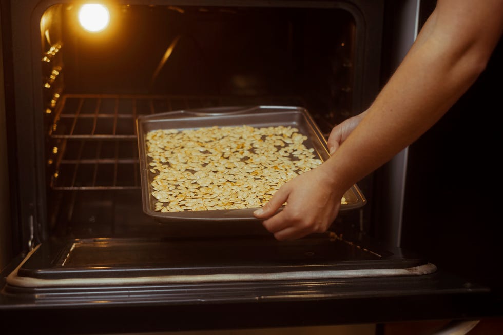 close up of a baking sheet full of pumpkin seeds being placed in a oven