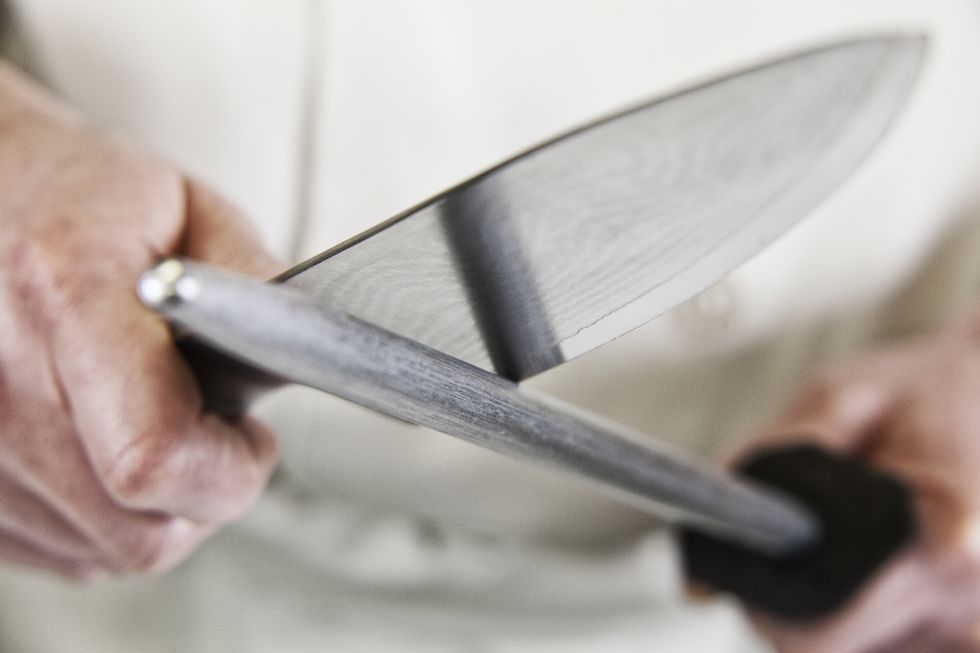 close up of a chef sharpening a large kitchen knife blade with a steel