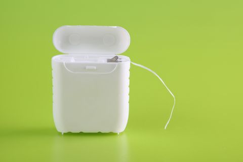 A close-up of a dental floss container on bright green
