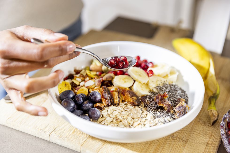 close up of a female hand eating a healthy bowl with various fruits, berries with chia seeds and nuts