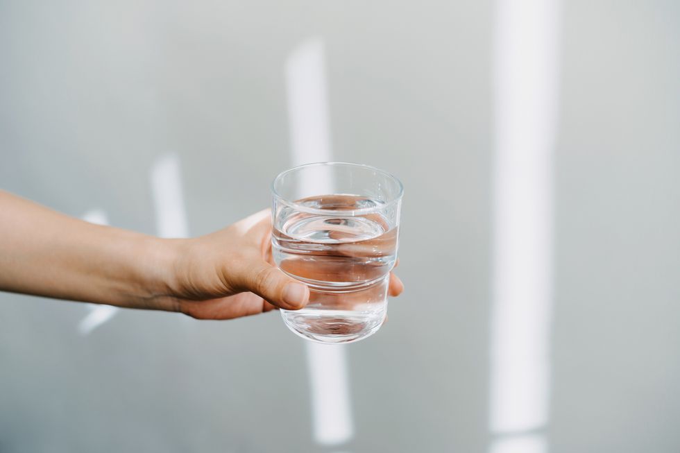 close up of a female hand holding a glass of water against white background with sunlight healthy lifestyle and stay hydrated