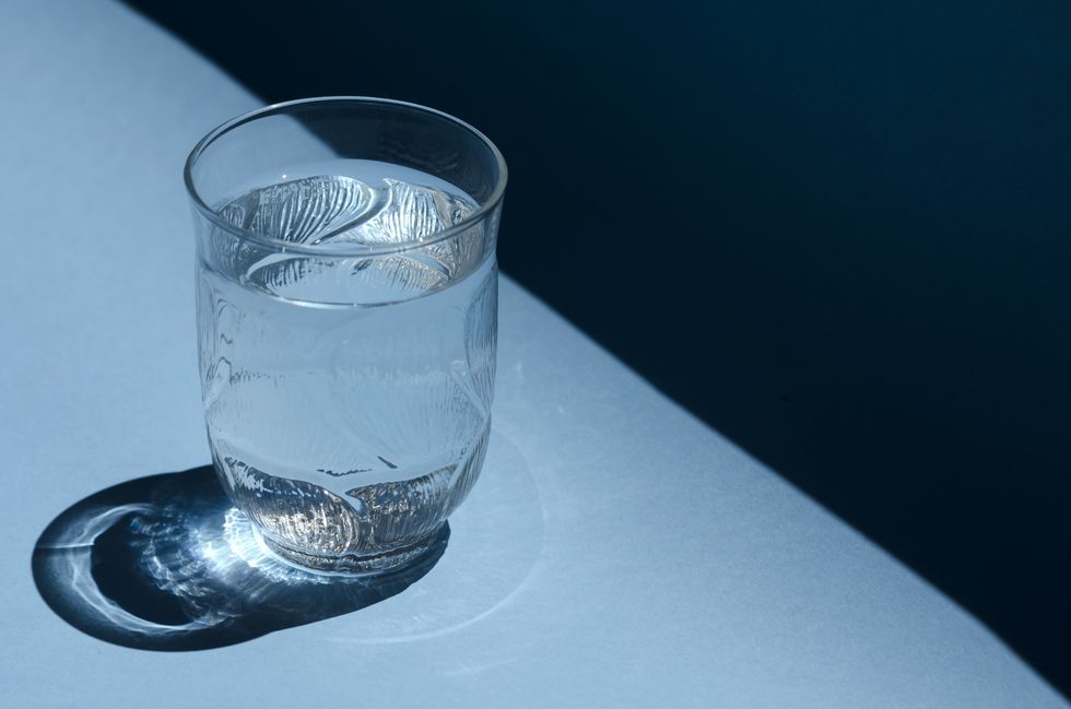 close up of a glass of water shining in the sunlight on a bright blue background
