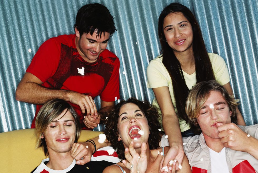 close-up of a group of friends sitting on a couch eating and throwing popcorn