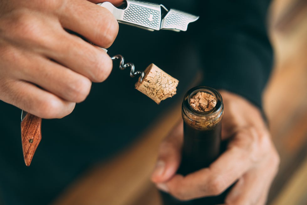 close up of a man's hands opening a wine bottle with a corkscrew, and a broken wine cork