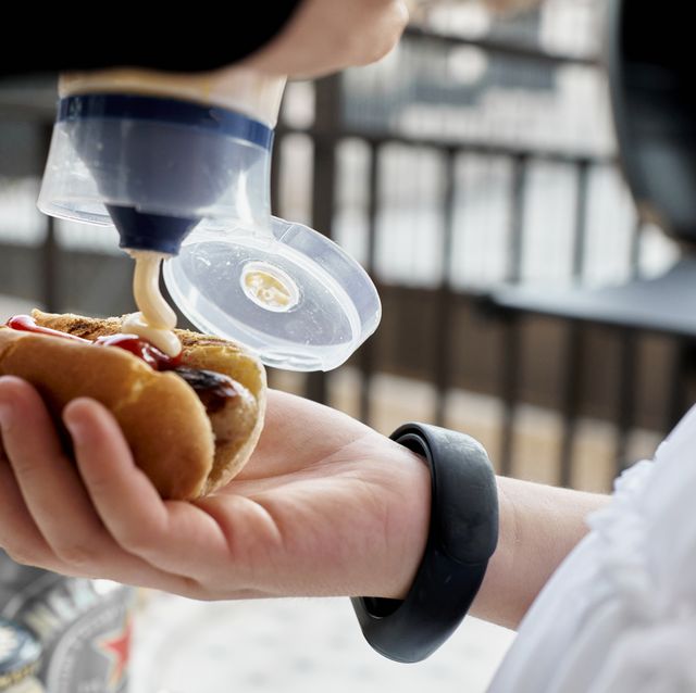 close up of a person dressed in white holding a hot dog while putting mayonnaise sauce on it and some bars in the background.
