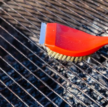 close up of a red brush with golden bristles and a scraper for cleaning a barbecue grill grate the concept of cleaning after lunch in open air, picnic, barbecue, lunch