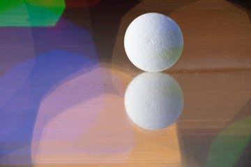 close up of a reflected pill on a reflective surface colorful lights background