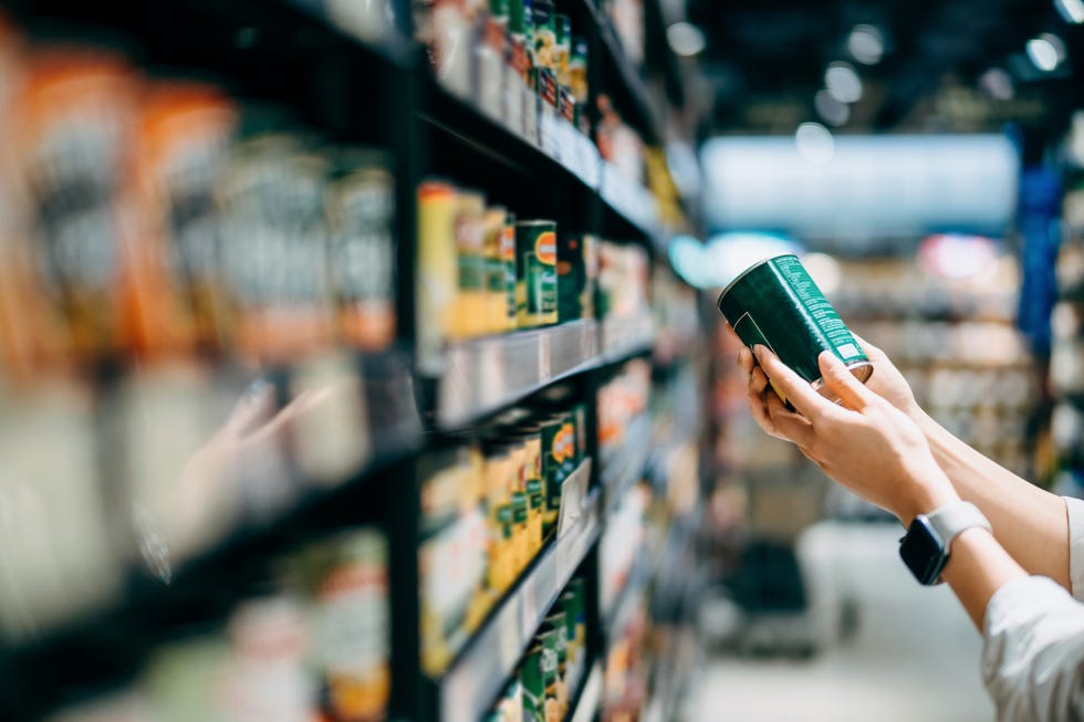close up of a woman grocery shopping in supermarket holding a tin can and reading the nutrition label at the back