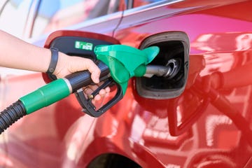 close up of a woman standing at a gas station filling her car with gasoline