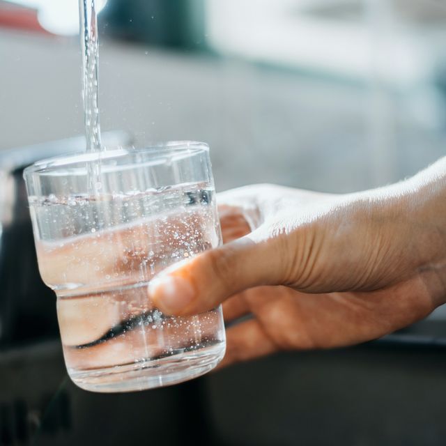 close up of a woman's hand filling a glass of filtered water right from the tap in the kitchen sink at home
