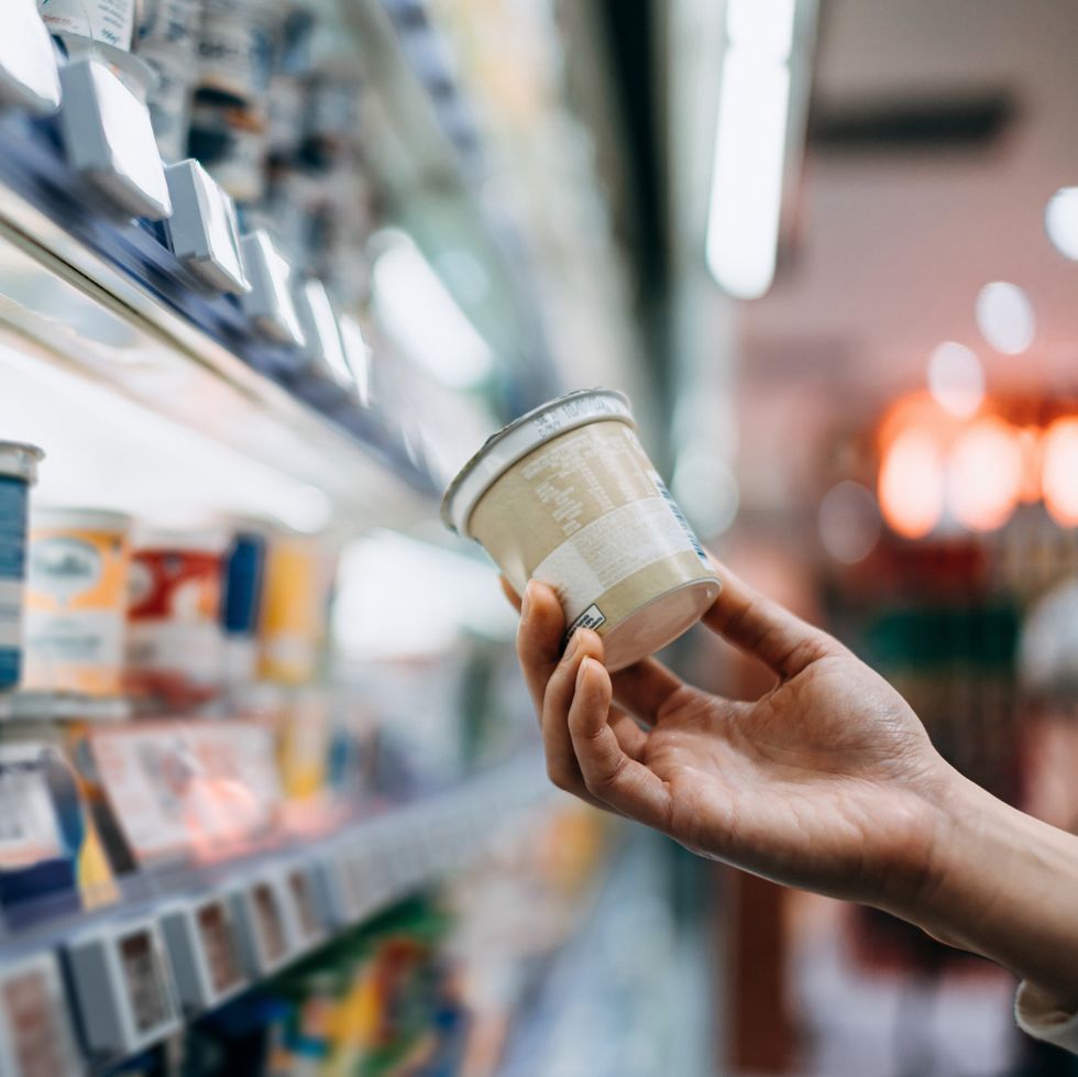 close up of a woman's hand shopping for fresh organic healthy yoghurt along the dairy aisle in supermarket, reading the nutrition label on the pot routine grocery shopping healthy eating lifestyle making healthier food choices smart eating concept