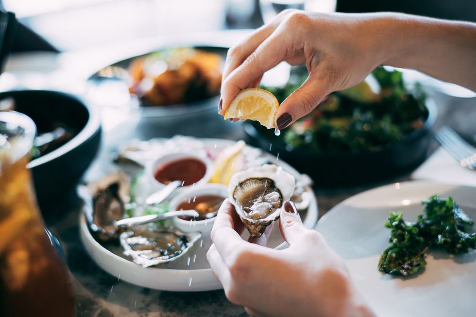 close up of a woman's hand squeezing lemon juice on to a fresh oyster, enjoying a scrumptious meal in a restaurant eating out lifestyle