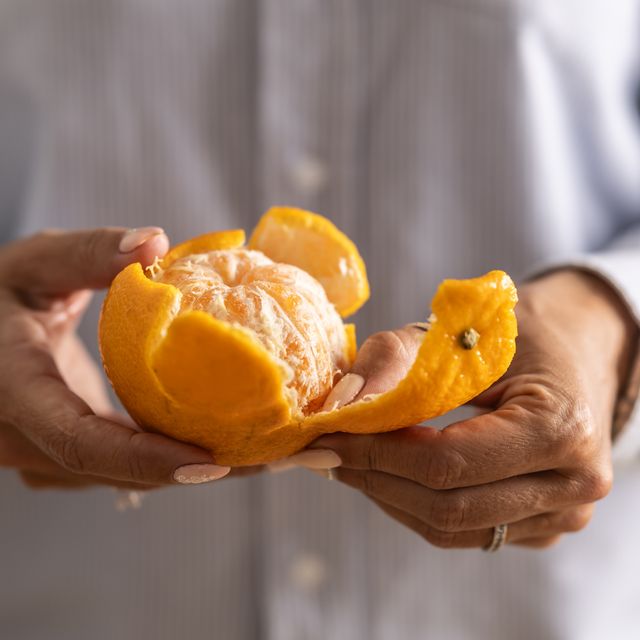 close up of a woman's hands peeling a tangerine