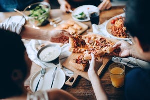 close up of a young group of friends passing and serving food while enjoying together they are having fun, chatting and feasting on food and drinks at dinner party