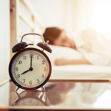 Close-Up Of Alarm Clock On Table By Woman Sleeping On Bed At Home