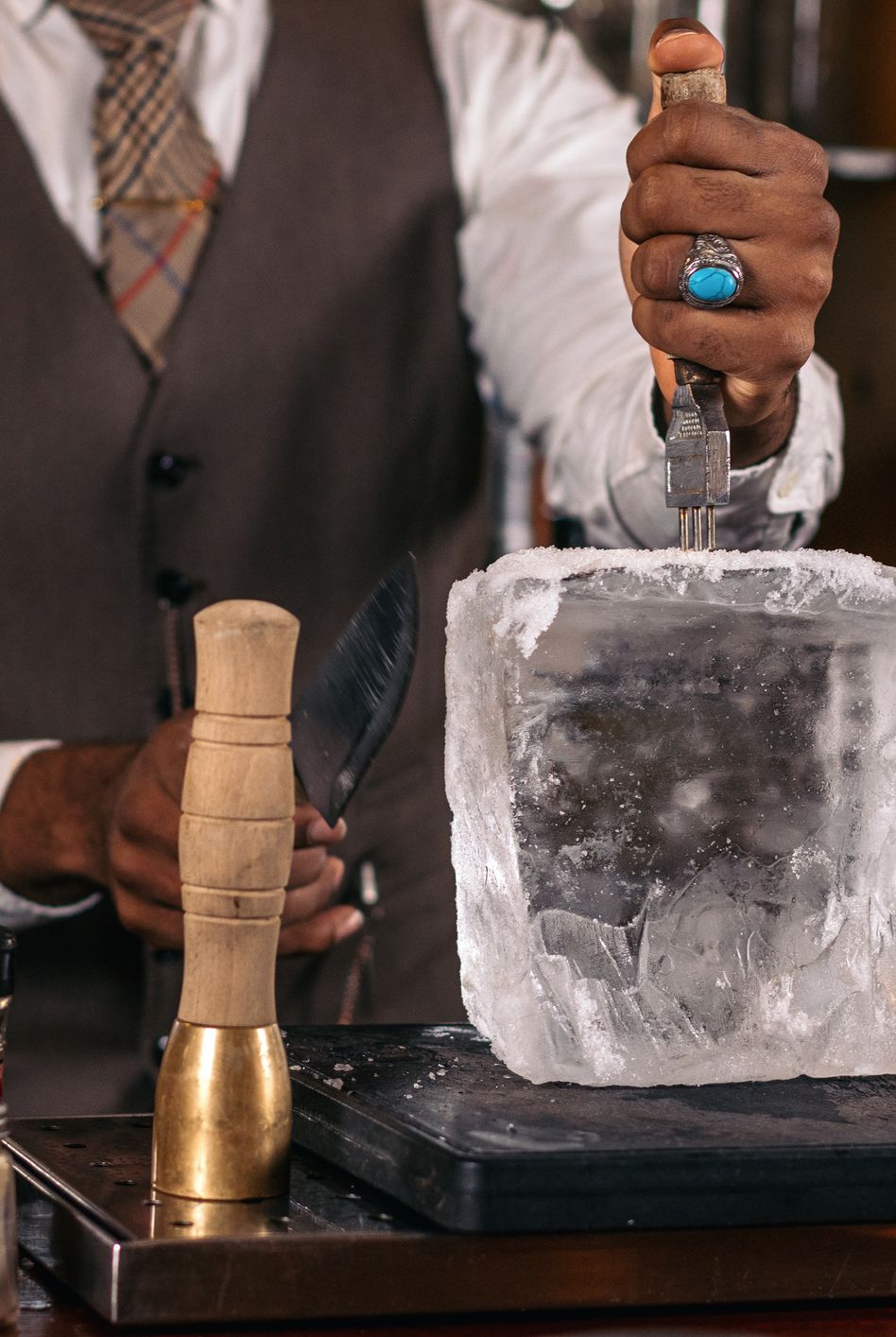 close up of an unrecognizable black bartender cutting a large ice cube to prepare a cocktail