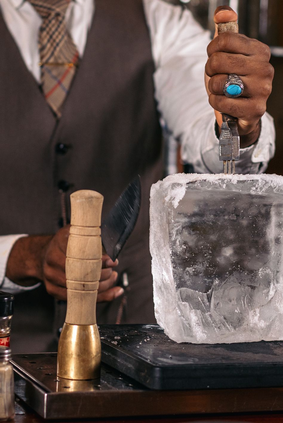 close up of an unrecognizable black bartender cutting a large ice cube to prepare a cocktail