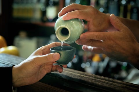 close up of bartender hand pouring sake to glass which hands of adult man