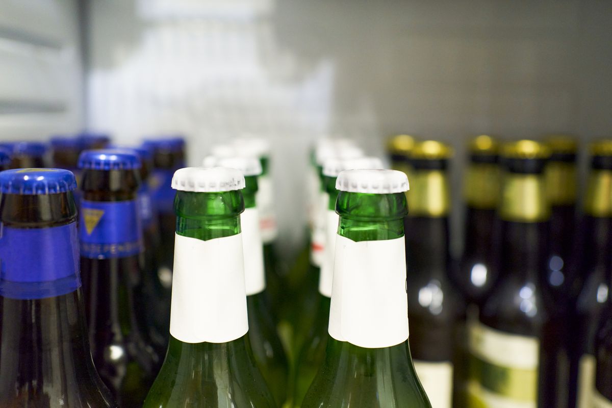 close up of beer bottles with white cap and beers with blue and gold details in the background inside the refrigerator