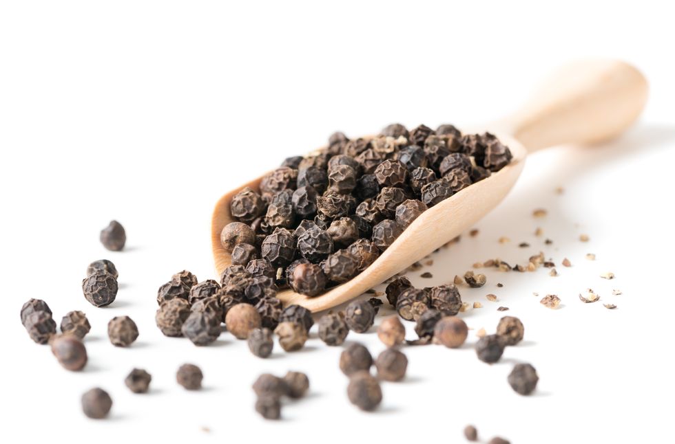 closeup of black peppercorns in wooden spoon over white background