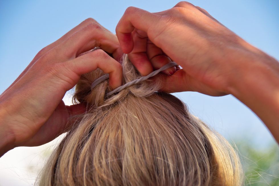 close up of blond woman tying hair with elastic against clear sky