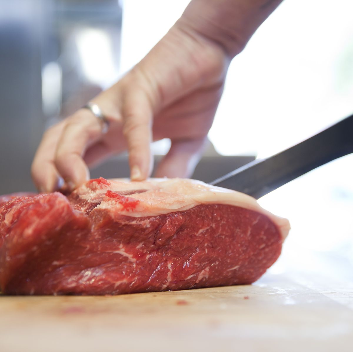Close up of butchers hands slicing raw steak on butchers block