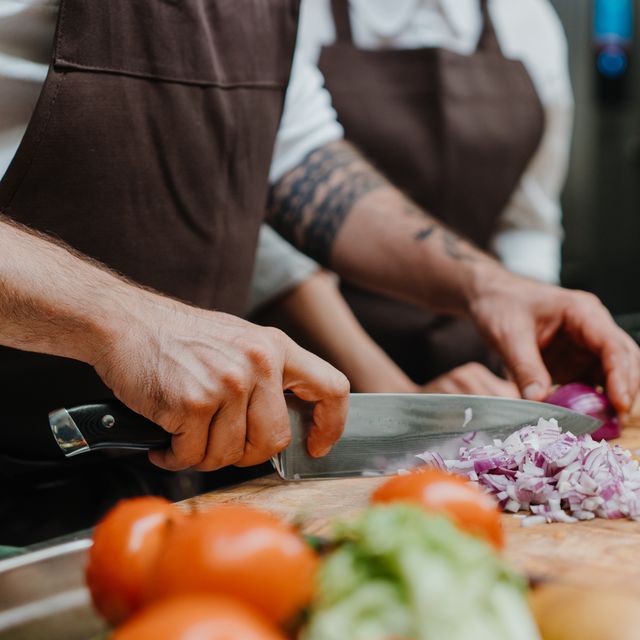 close up of chef cutting onion on cutting board in restaurant kitchen