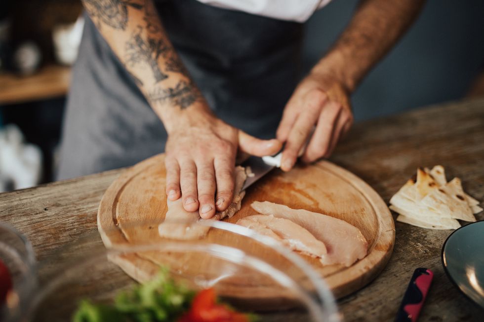 close up of chef's hands cutting chicken meat on the wooden board