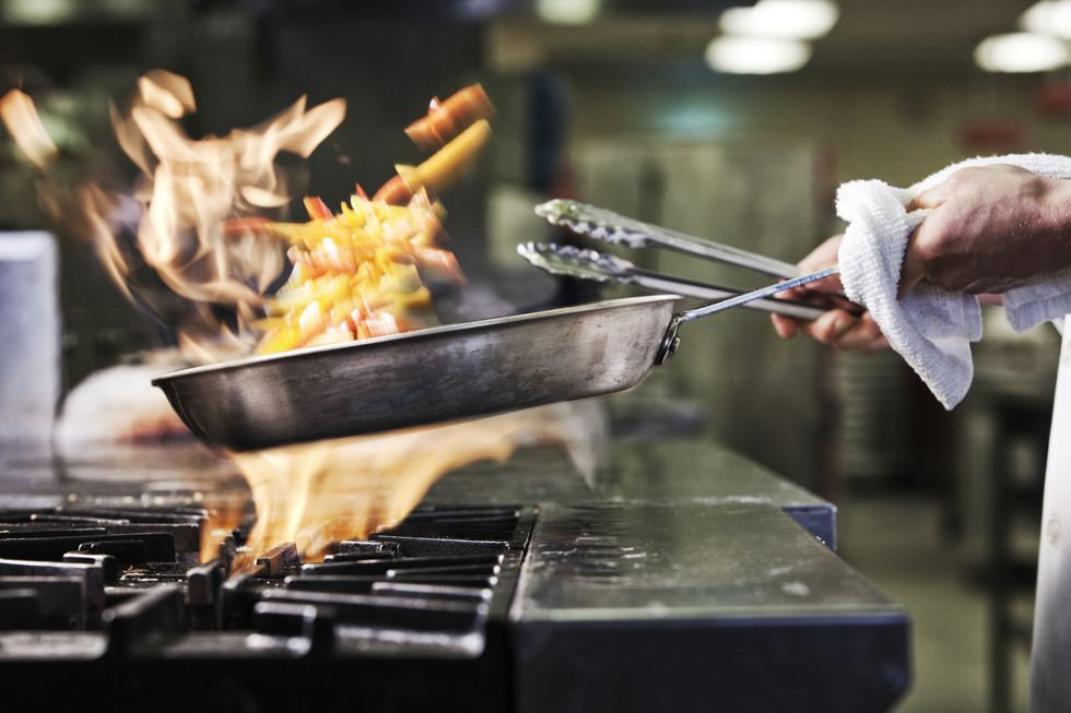 Close-up of chefs hands holding a saute pan to cook food, flambeing contents. Flames rising from the pan.