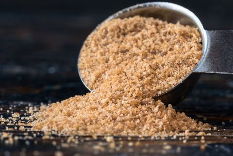 a measuring spoon of coconut sugar on a table, an ingredient in one of good housekeeping's best homemade face scrubs