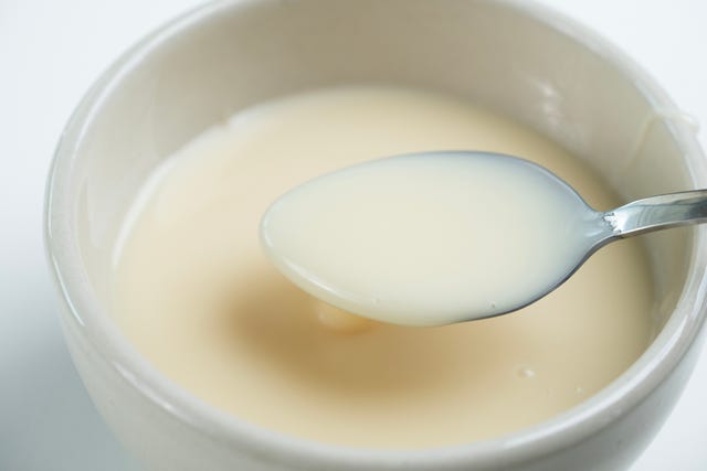 close up of condensed milk with spoon isolated on white background, food ingredients concept