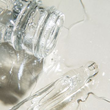 close up of drops of facial serum or essential oil pouring out of glass bottle nearby pipette on beige background